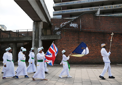 A colour photograph of a group of people wearing white and holding flags while walking along a path.