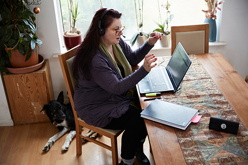 A photograph of a person at their laptop with a headset on, taking part in an online meeting.