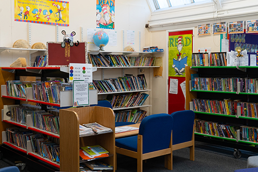 A photograph of a library or reading area, full of bookshelves with books, learning resources and chairs.