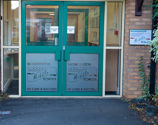 A photograph of Monkseaton Middle School entrance doors. ‘To care & succeed’ is printed on the doors.