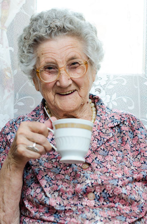 An older lady smiling and holding a tea cup in her hand.