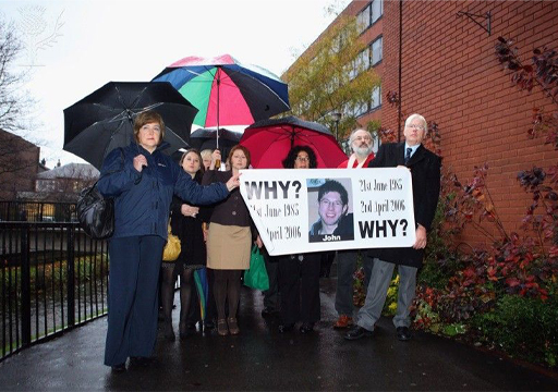 A group holding a banner with ‘Why?’, the dates 21 June 1986 and 4 April 2006, and a photo of a man with the name John written under it.