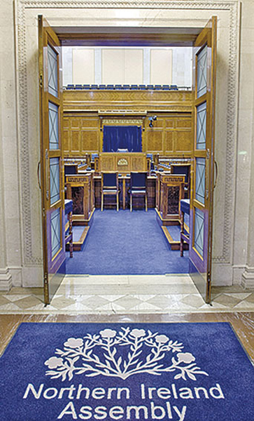 Photo of a council chamber, with a rug entitled ‘Northern Ireland Assembly’ at the entrance.