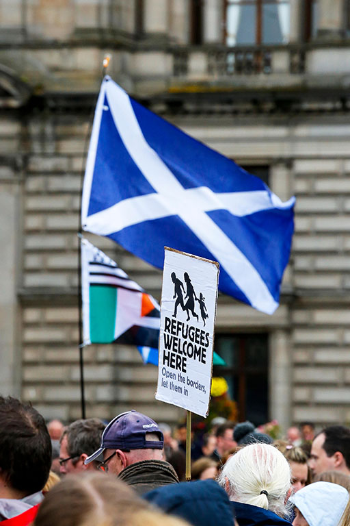 Photograph of a demonstration with the Scottish flag and a placard which reads ‘Refugees Welcome Here’.