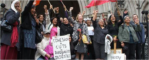Group of women with arms raised punching the air. A sign is held which reads ‘Cohesion + cuts = Inequality + Injustice’.