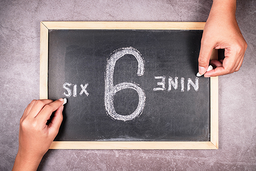6/9 written on a blackboard. An arm coming from the bottom of the image writes six, an arm from the top writes nine.
