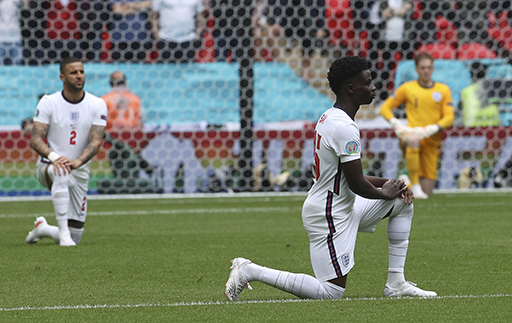 A photograph of three England footballers taking the knee on the pitch.