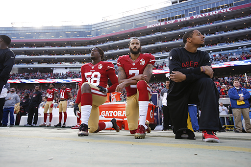 A photograph of three American footballers taking the knee in a stadium.