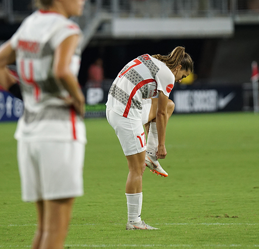 A photograph of a footballer tying the laces on her football boot.