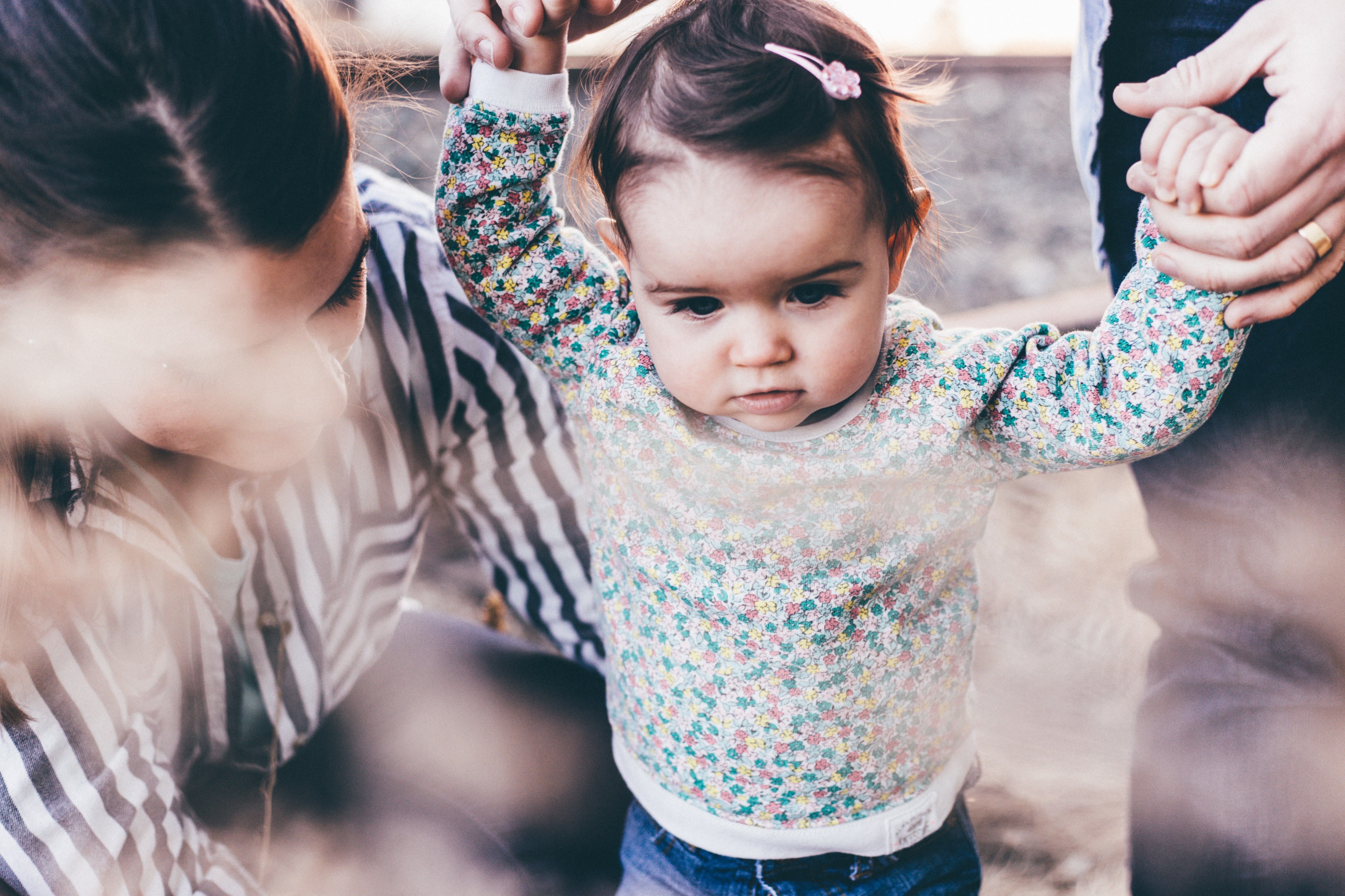 Women holding a girl learning to walk.