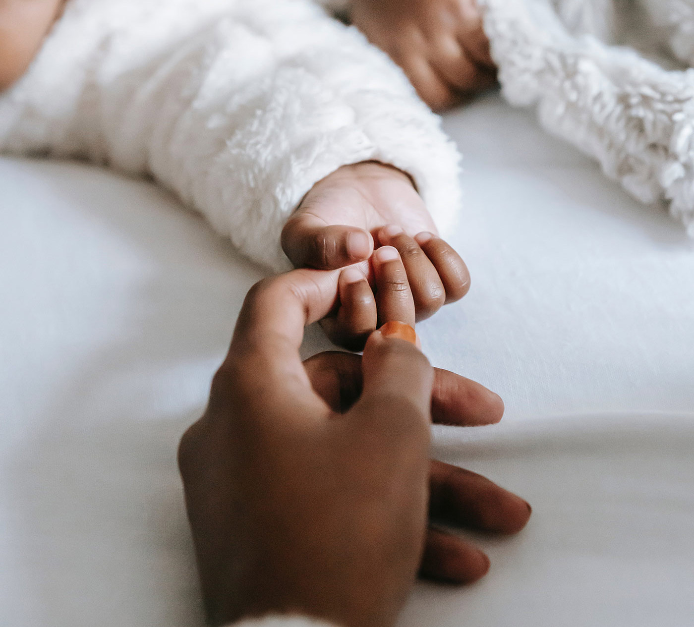 Mother holding hand of baby lying on bed.
