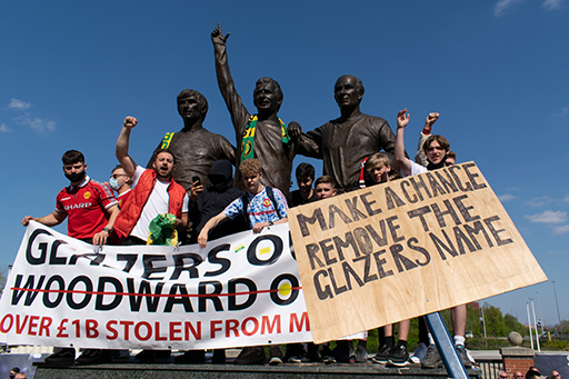 A photograph of a group of fans holding signs saying ‘Glazers out, Woodward out’ and ‘Make a change, remove the Glazers name’.