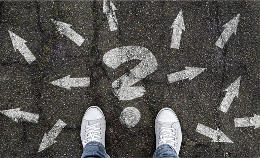 Photograph of shoes on the ground with a question mark painted on the floor and arrows going in different directions.