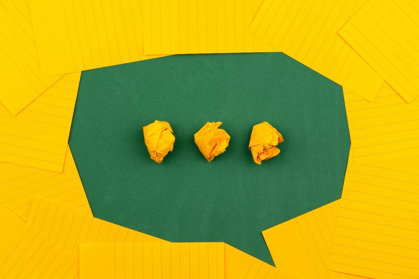 Image to represent communication. Yellow background, green speech bubble with three scrunched up pieces of yellow paper