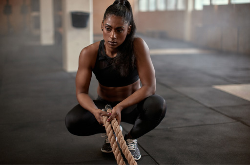 The image shows a female in sportswear holding onto two ropes. She looks tired and deep in thought.
