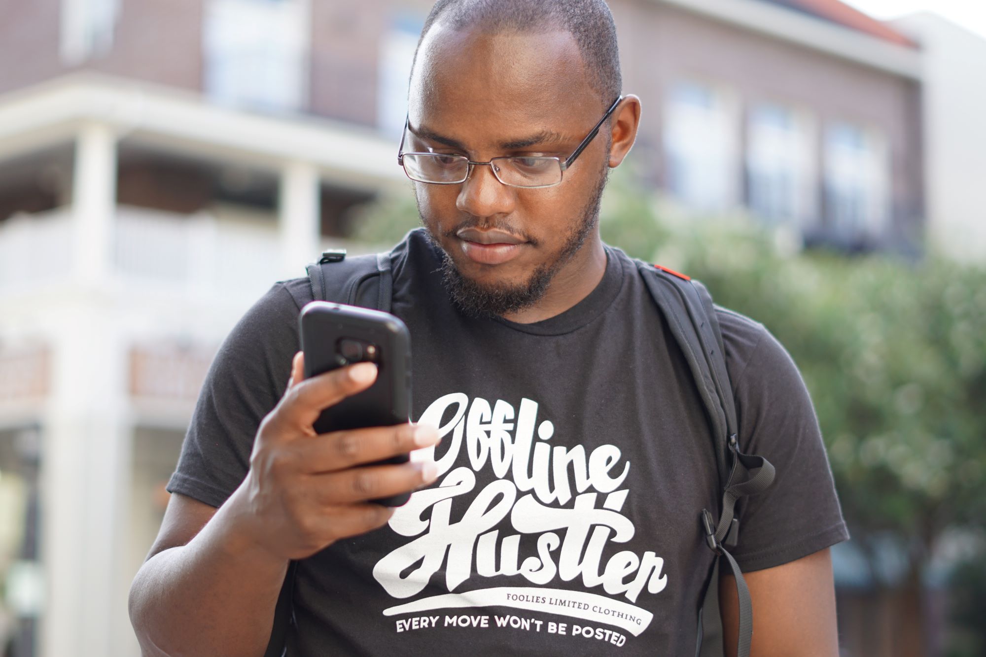 Young black guy, casually dressed in a brown T-shirt, looking at a smart  phone.