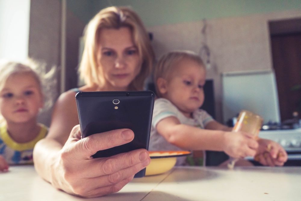 Stressed woman, looking at her mobile phone with a child on both sides
