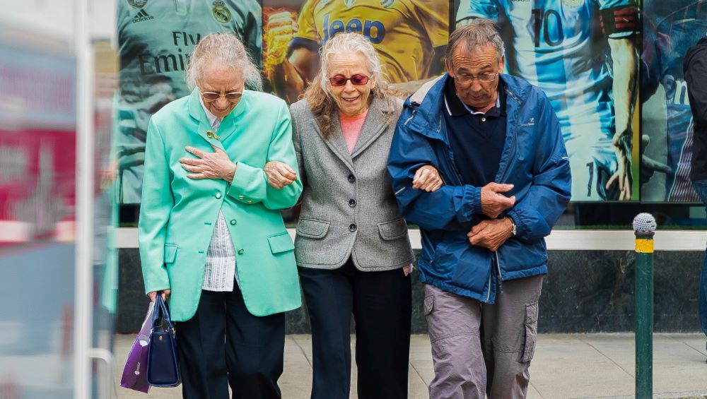 three seniors linking arms to cross a road, two women and one man