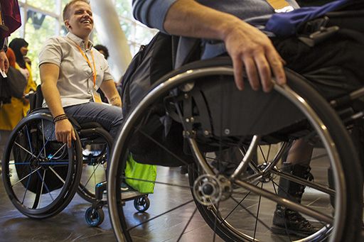 A photograph of two people in wheelchairs in an open space, seemingly on the move.