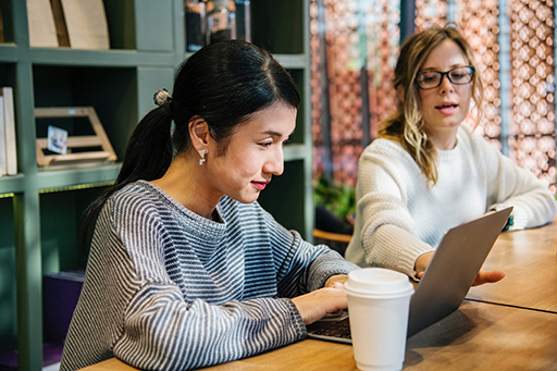 A photograph of two people working on a laptop.