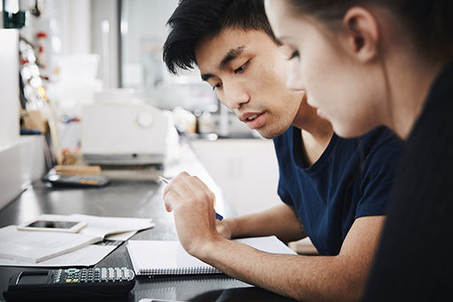 A photograph of two people studying some calculations with a calculator and notepad.