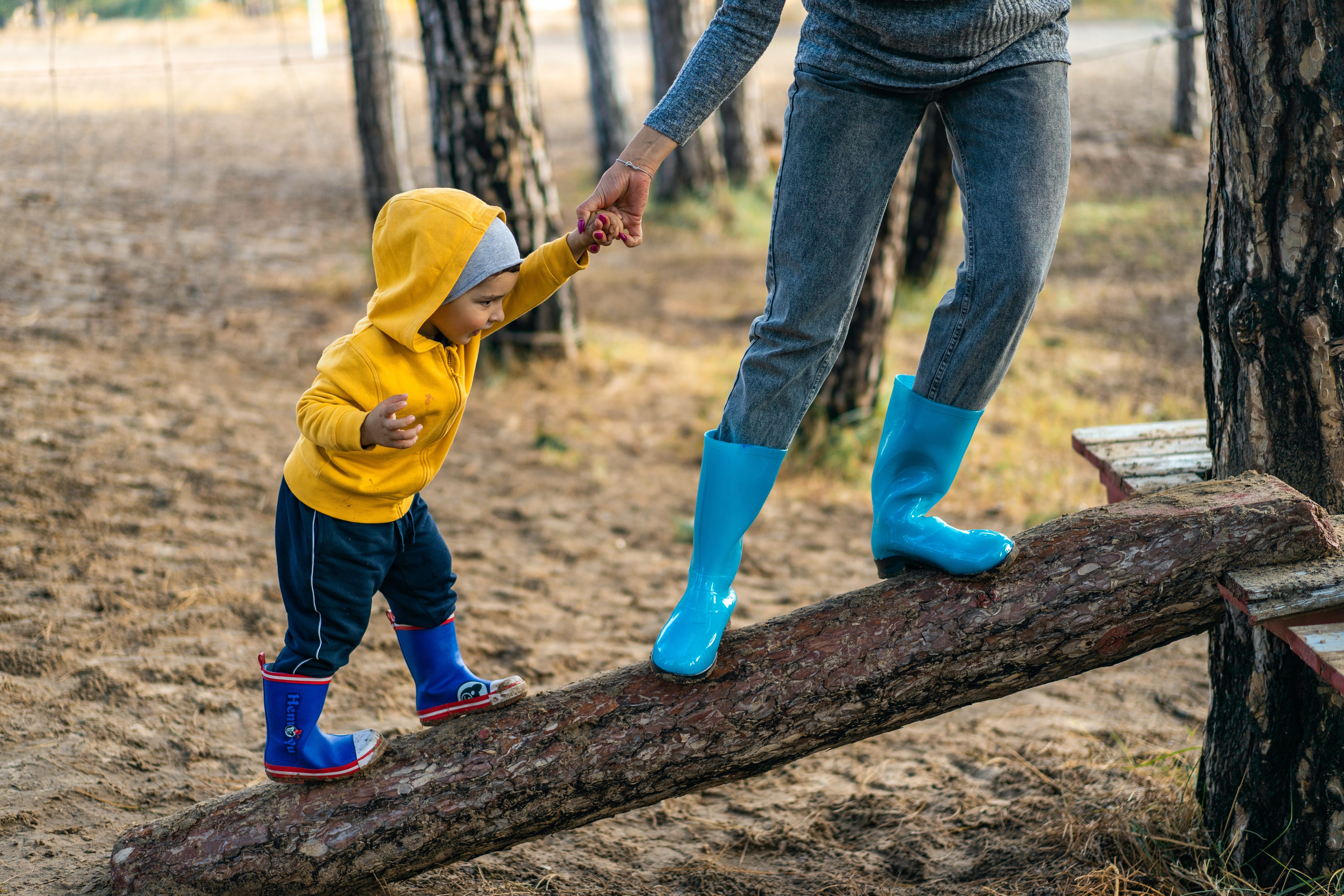 Small child in yellow jacket walking up a ramp, adult holding a hand