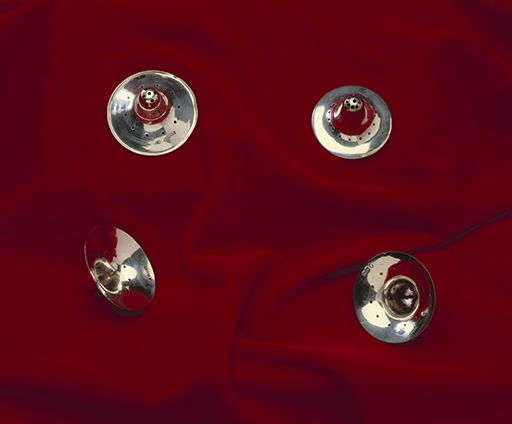 This coloured photograph shows four silver metallic objects lying on red fabric. Each of the four objects is circular with a small opening in the centre.