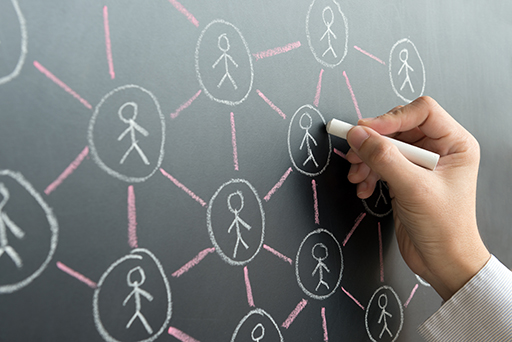 Photograph of a hand writing on the chalkboard. They are drawing a network of people.