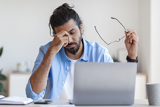 Photograph of a person at a laptop looking fatigued.
