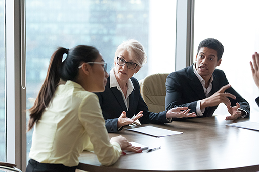 A photograph of three people talking around a table.