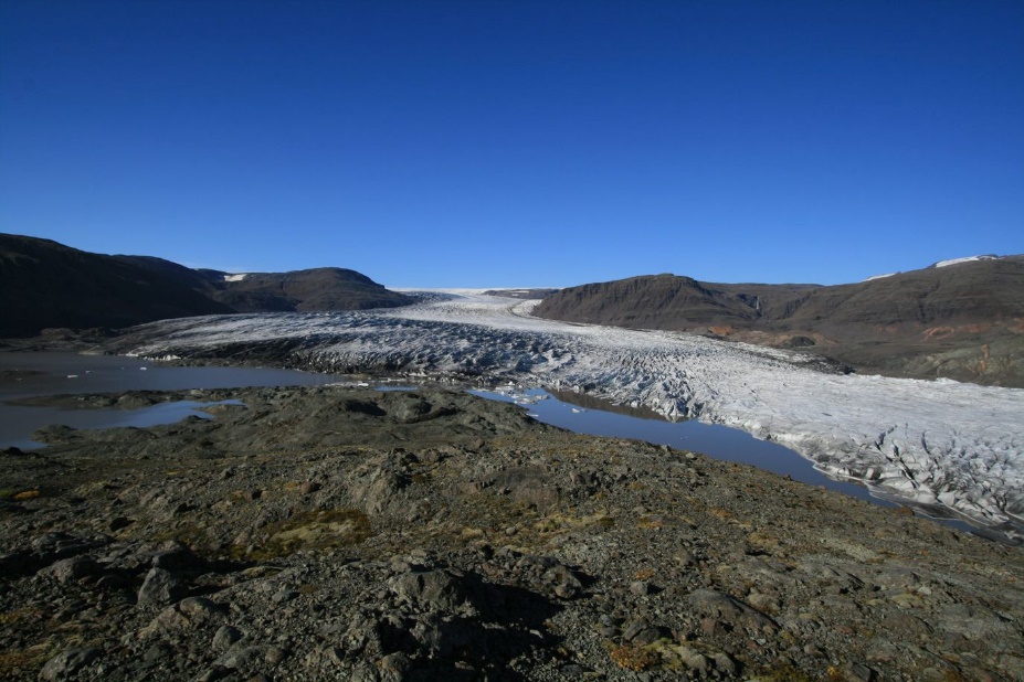 View over a valley in Iceland. A glacier of dirty white ice partly fills the valley; in the foreground the glacier melted.