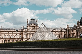 A palatial building with a large glass pyramid before it.