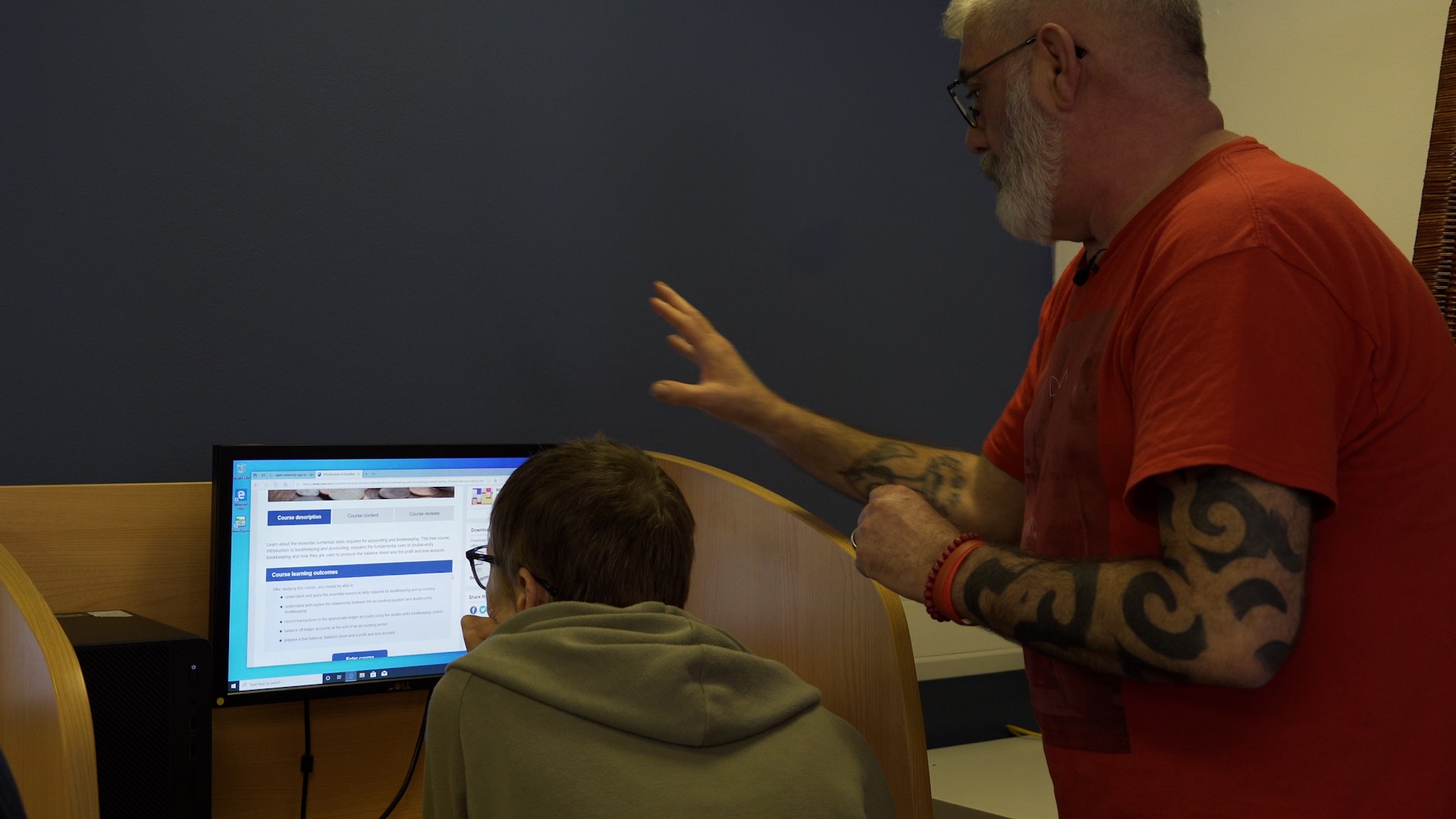 Tony collins-moore standing behind a seated carer, both are looking at a computer screen. 
