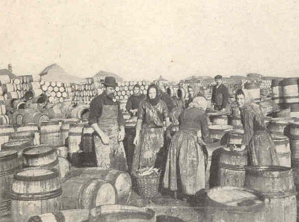 A scene showing men and women next to barrels of herring