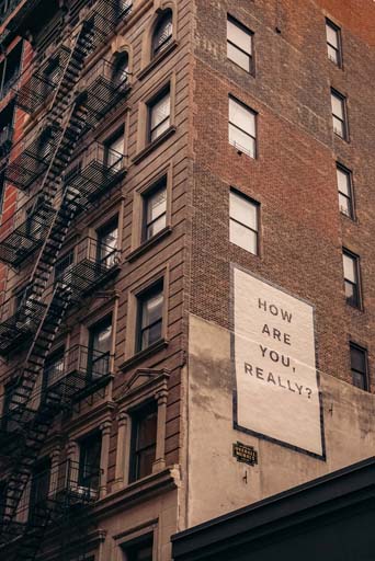 A tall brick building with a poster on the side with the text ‘How are you, really?’