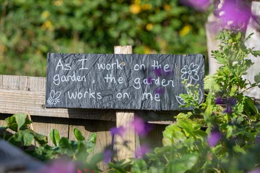 A sign in a garden saying ‘As I work on the garden, the garden works on me.’