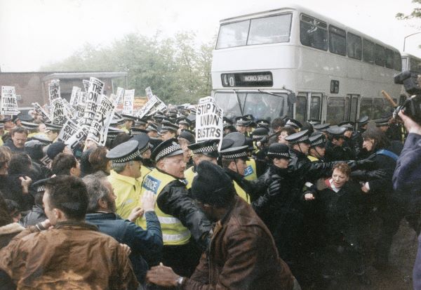 Protestors on a picket line fighting with police as a bus attempts to get through the crowd