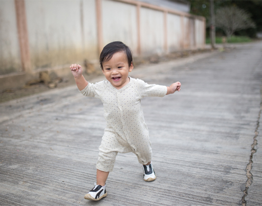 A toddler smiling and running along a path.