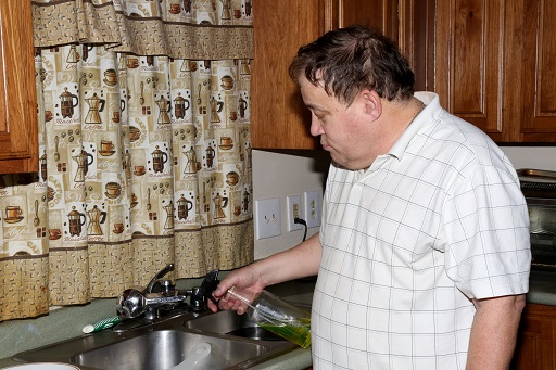 A photograph of a man in a kitchen cleaning the sink.