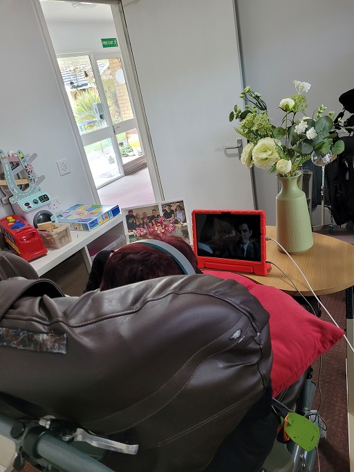 Photograph of Susie sitting in her wheelchair watching television on a tablet.