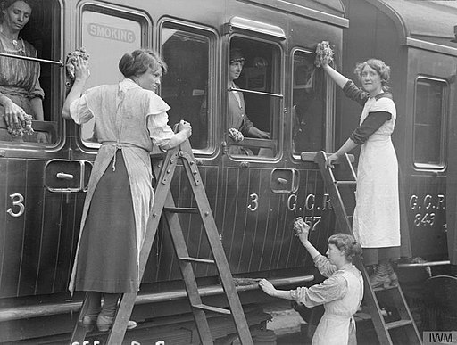 Three ladies, two on ladders, cleaning a train. One is looking at the camera and smiling.