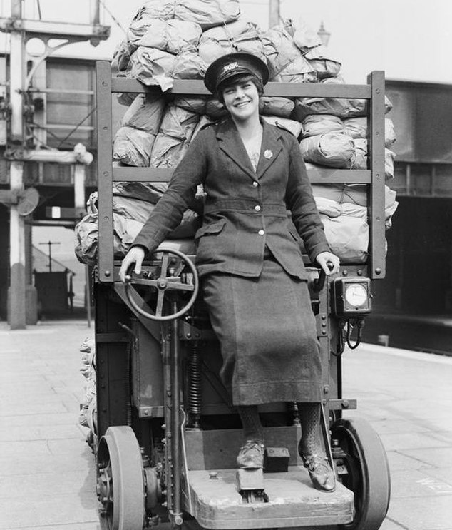 A women worker on the railways, first world war, sitting in front of a cargo vehicle, uniform, wearing a cap and smiling.