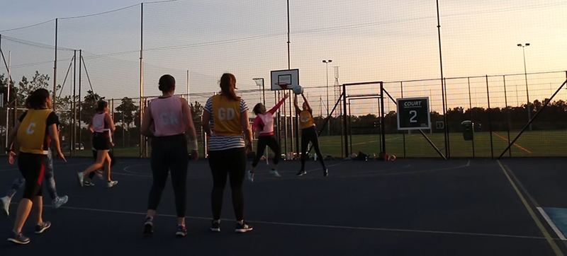 A photograph of people playing a game of netball on a netball court.