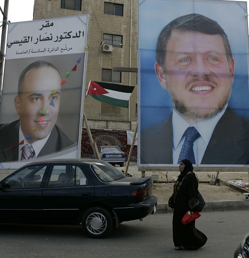 This image shows two large posters mounted on a street in a built-up area. The poster on the right depicts the head, shoulders, neck and chest of a middle-aged man wearing a business suit. He wears a short beard.