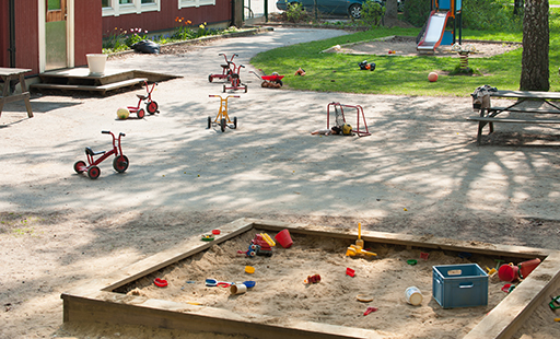 An outdoor play area with a sand pit, trikes and slide