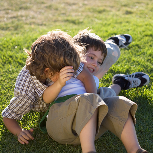Two children playing rough and tumble on grass