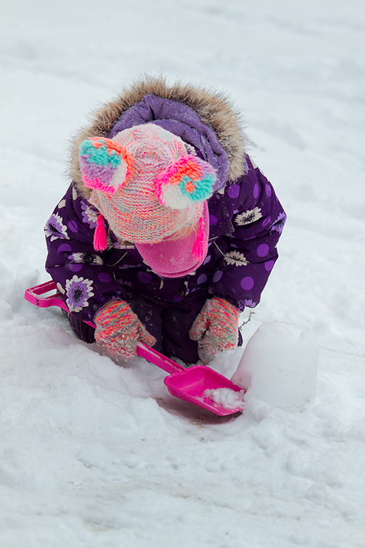 A child outside in winter wear scooping up snow