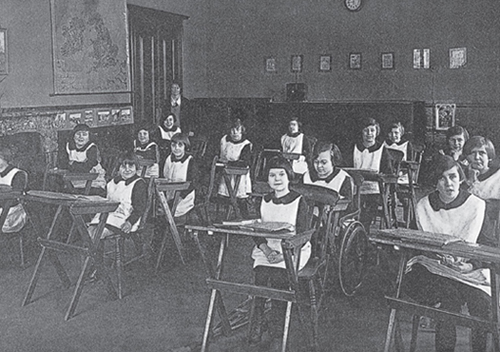 This is a black-and-white photograph of a group of young children sitting at desks.