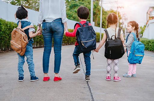 Three children and one adult walking hand in hand in a line facing away from the camera