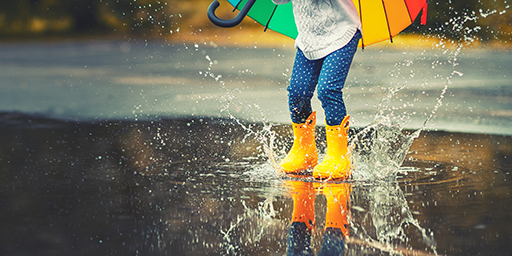 The legs of a child wearing wellies splashing in a puddle